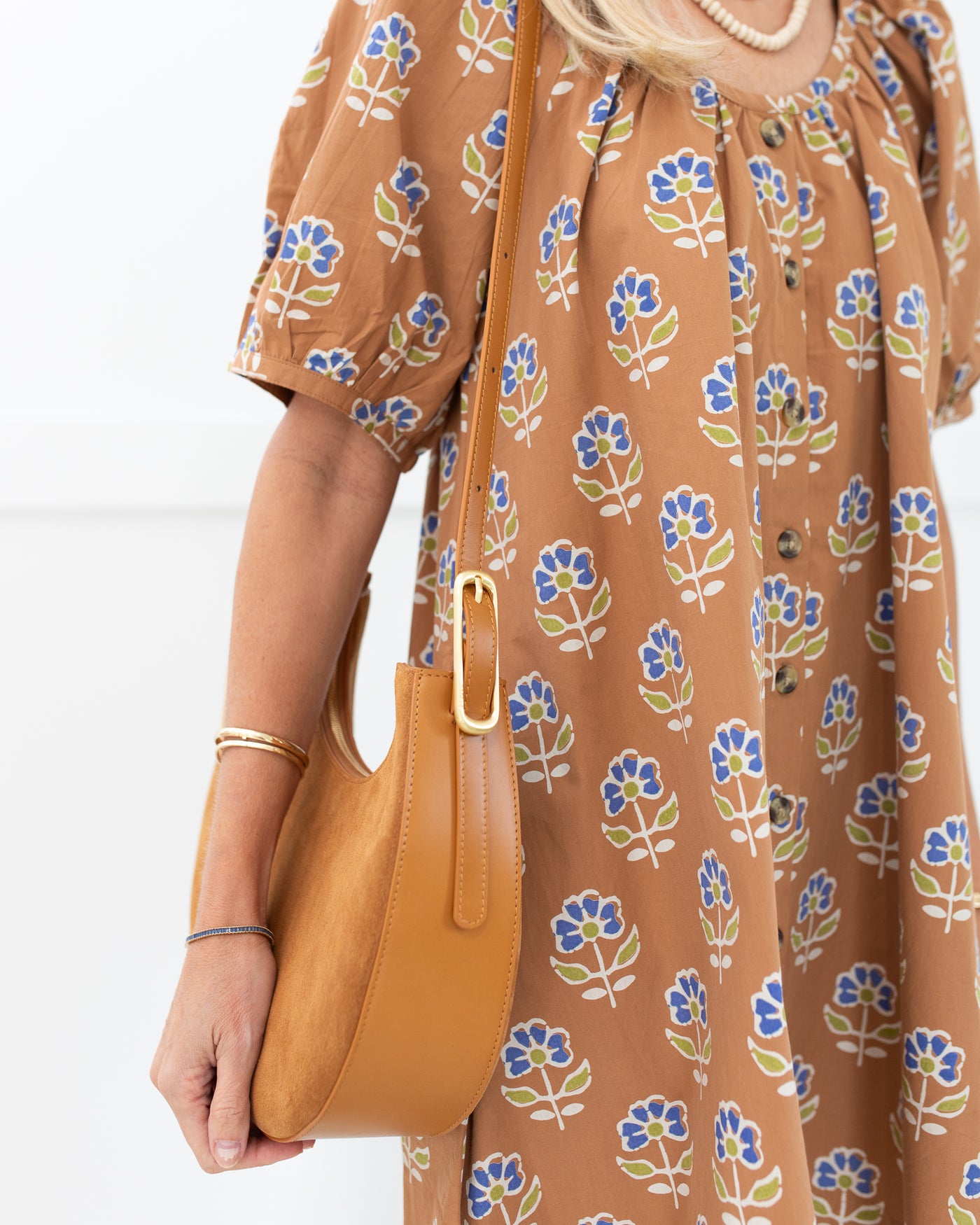 Woman holding a tan handbag wearing a brown dress with floral pattern

