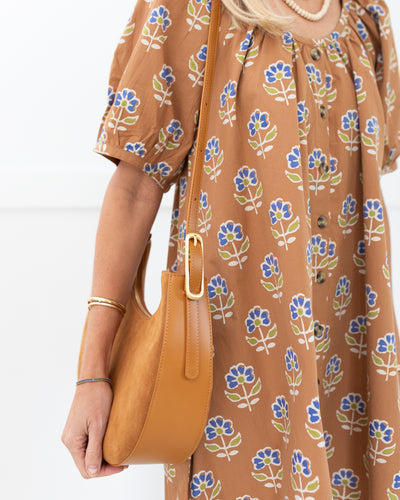 Woman holding a tan handbag wearing a brown dress with floral pattern

