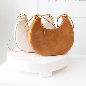 Two handbags, one white and one brown, on a white surface with a blurred background.